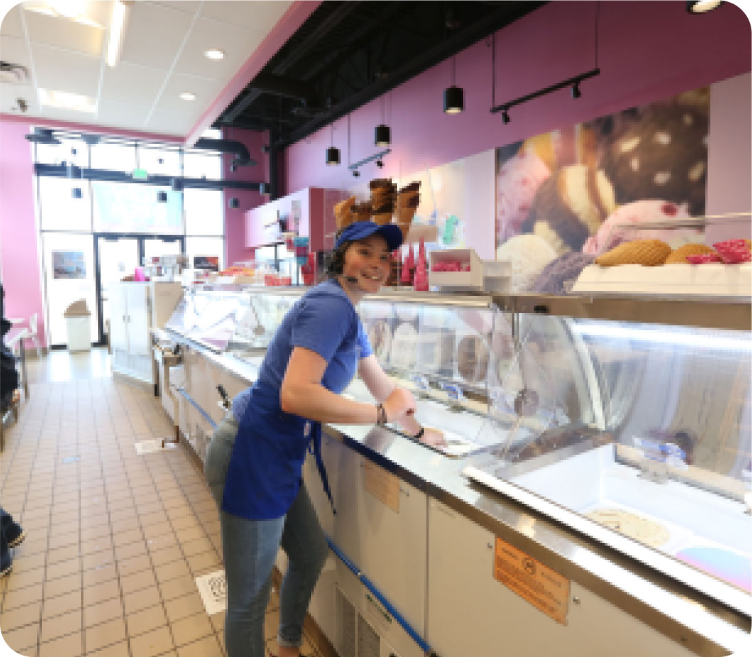 A cheerful employee scooping ice cream at a brightly colored ice cream parlor.