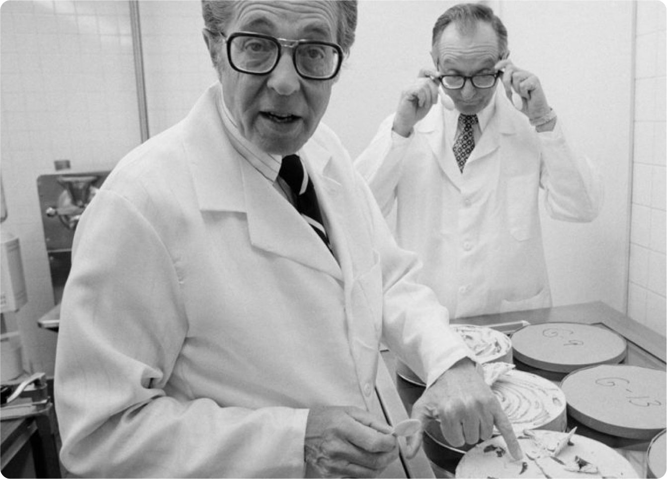 Two elderly male scientists in lab coats examining brain models in a laboratory setting. one is adjusting his glasses, the other pointing at a model.