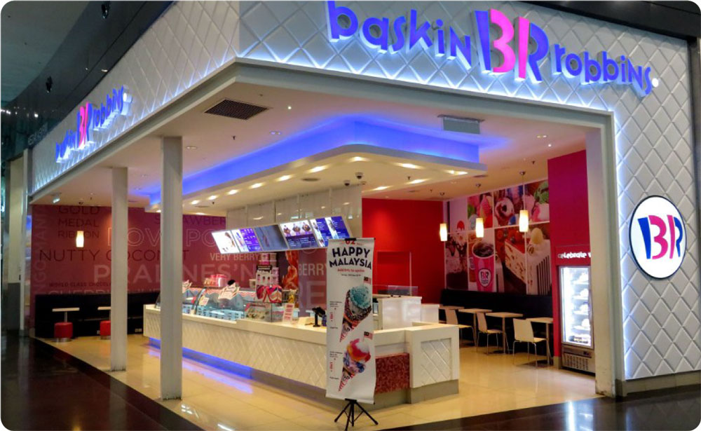 A well-lit baskin-robbins ice cream store entrance in a mall, featuring a bright neon sign and a view of the ice cream counter inside.