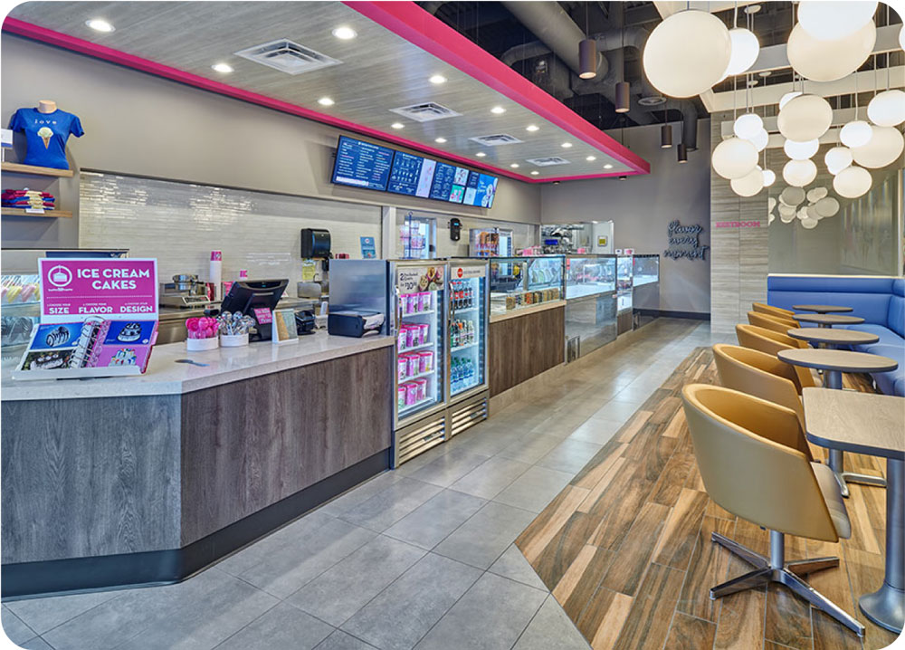 Modern ice cream parlor interior with a bright, clean design featuring a counter, digital menu, seating area, and hanging round lights.