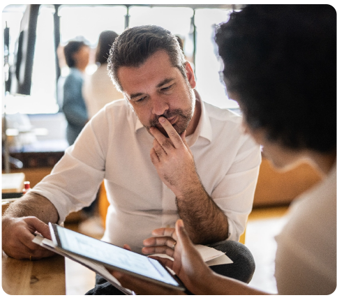 Two men in a business meeting, one listening intently while touching his chin, the other holding a digital tablet.